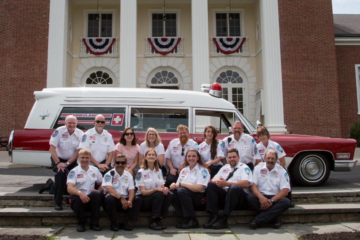 Memorial Day Parade 2016 - 2 rows of men sitting on steps with vintage ambulance behind - behind ambulance is Town Hall 