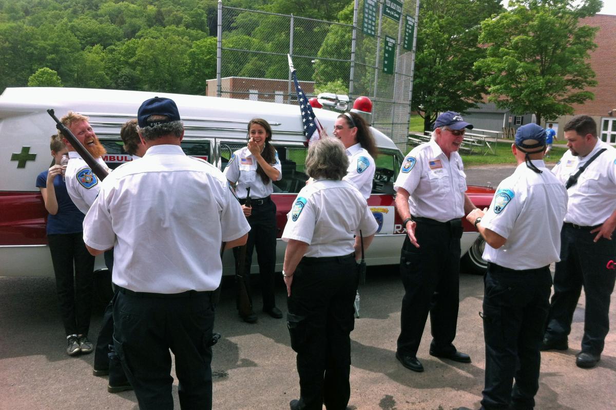 Memorial Day Parade 2016 - large group of men in white shirts, black pants mingling near vintage ambulance