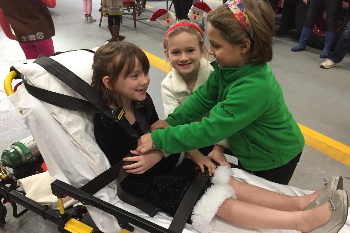 Brownie Troop #40226 visit 2016 - young girl pretending to be patient on gurney, 2 girls at her side, one strapping her in