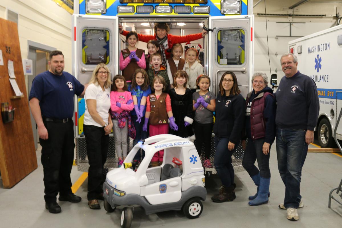Approximately 10 people from Brownie Troop #40226 standing in a row facing forward behind toy mini-ambulance