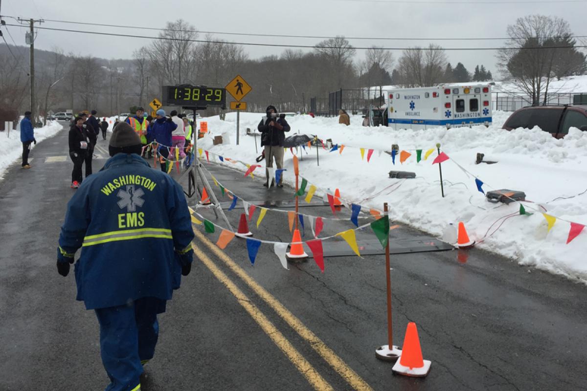 Polar Bear Run standby 2015 - peple milling near stand of flags on strings at side of road, snow on both side of road