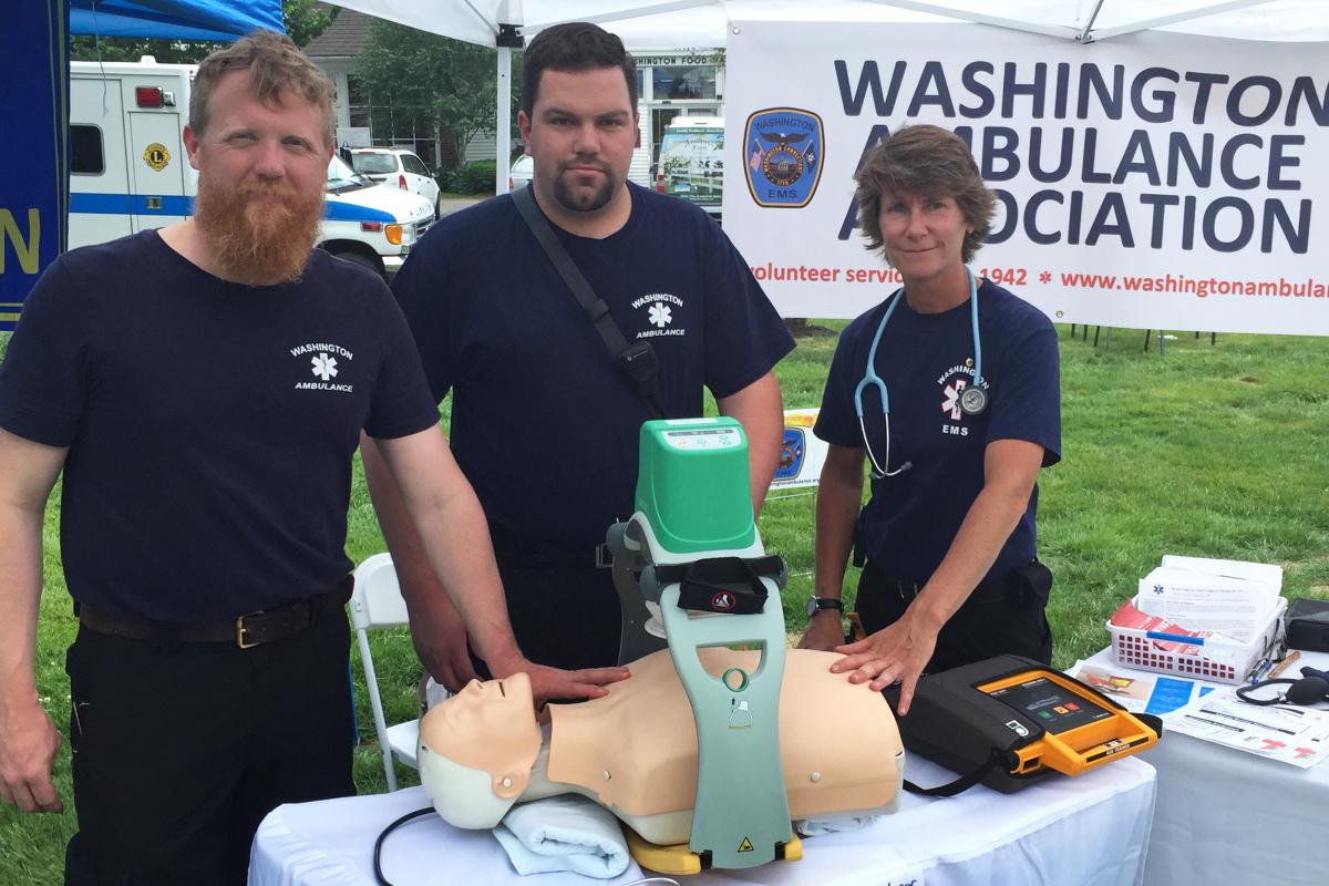 Community Day 6/4/2016 - 3 people stnading behidn thable with hands on mannequin. Sign "Washington Ambulance Association"